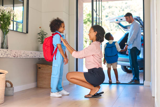 Woman helping a child with a backpack as another child waits by a car.